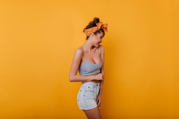 Stunning slim female model with orange ribbon in hair posing on yellow space