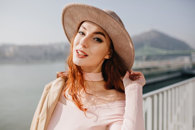 Stunning white woman in fedora relaxing near sea in cold day