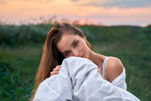 Stunning woman posing on field with white blanket in hands