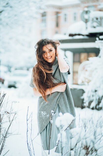 Stunning woman in a sweater and light dress stands in the garden among bushes 