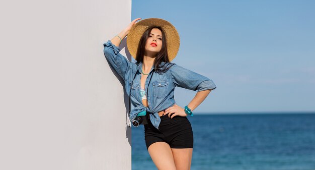 Stunning woman with figure in shorts and straw hat posing on the beach.
