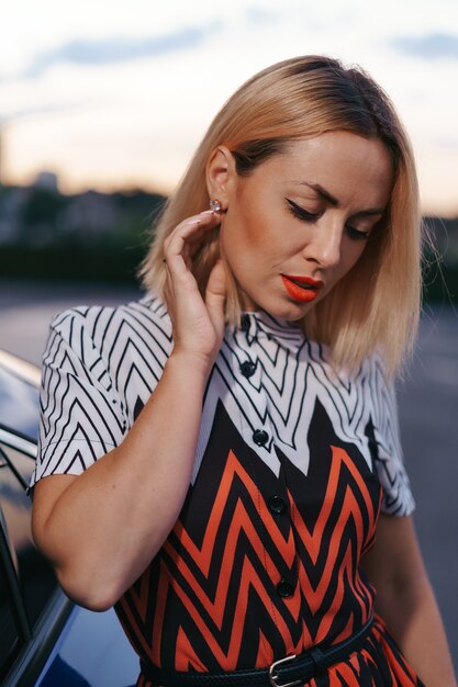 Stunning young woman close up portrait posing in front of her car outdoors, ownership driver