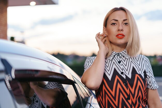 Stunning young woman close up portrait posing in front of her car outdoors, ownership driver