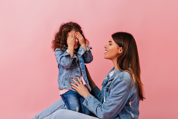 Stunning young woman playing with preteen kid. Studio shot of carefree family in denim clothes.