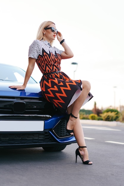 Stunning young woman waring dress posing in front of her car outdoors, ownership driver
