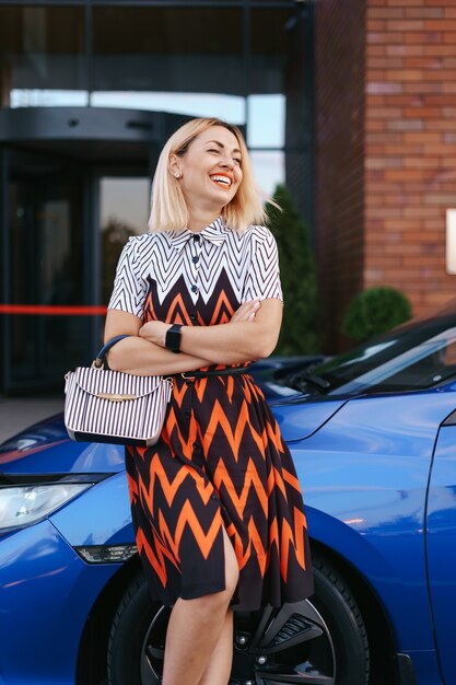 Stunning young woman waring dress posing in front of her car outdoors, ownership driver