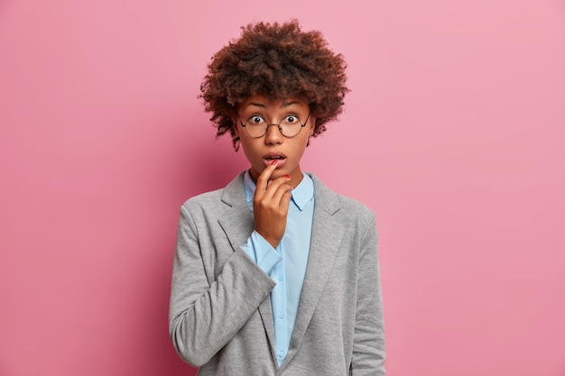 Stupefied African American female manager in formal outfit keeps mouth opened stares surprised at camera