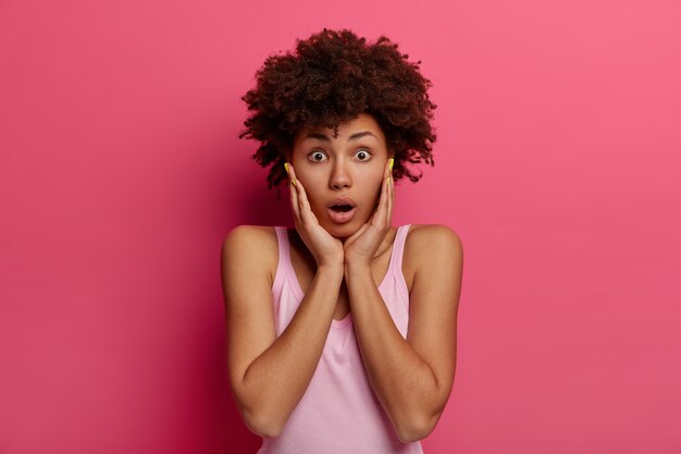 Stupefied emotional African American woman touches cheeks with hands