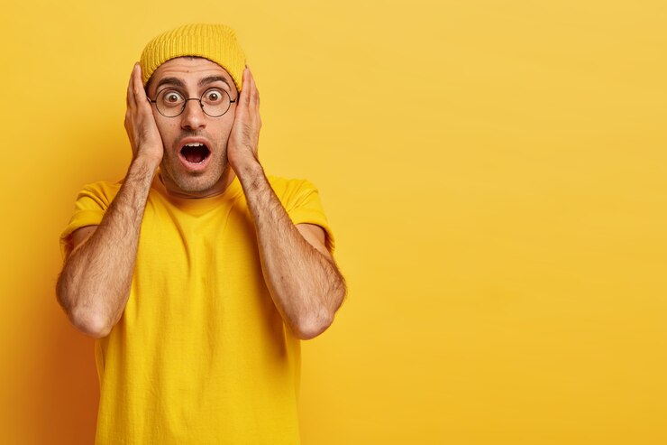 Free Photo stupefied emotional european man keeps hands on face, mouth widely opened, cannot believe in shocking relevation, wears vivid yellow clothes, being very emotional. omg concept