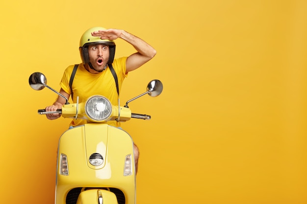 Stupefied guy with helmet driving yellow scooter