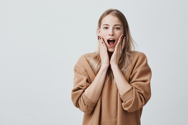 Stupefied stunned blonde woman keeps mouth widely opened