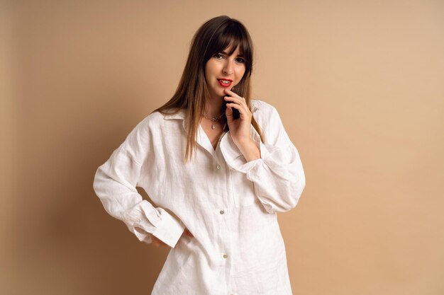 Stusio portrait of trendy brunette woman wearing white linen suit posing at beige background blogger fashionista