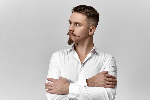 스타일, 패션 및 비즈니스 개념. 세련 된 콧수염과 그의 가슴에 팔을 교차 하 고 멀리 찾고, 사려 깊은 표정을 가진 수염을 가진 자신감 우아한 젊은 유럽 사업가의 스튜디오 이미지