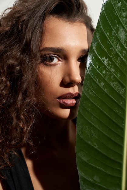 Free photo stylidh woman hiding face behind big green leaf