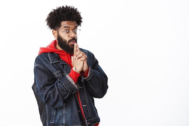 Stylish african-american bearded guy in transparent glasses blowing at gun, making pistol with hands, folding lips and holding hands near mouth as if making shot and looking at camera