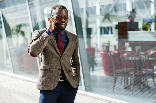 スタイリッシュなアフリカ系アメリカ人の黒人のビジネスマンがスマートフォンを立てて話す