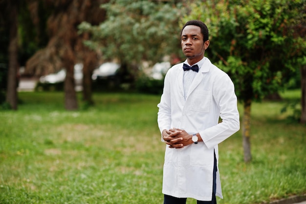 Стильный афроамериканский врач с бабочкой и лабораторным халатом позирует на улице