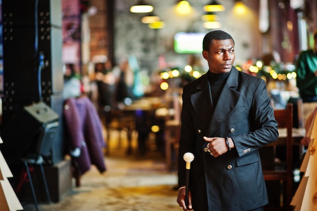 Stylish african american gentleman in elegant black jacket holding retro walking stick as cane flask or tippling cane with golden diamond ball handle Rich fashionable afro man