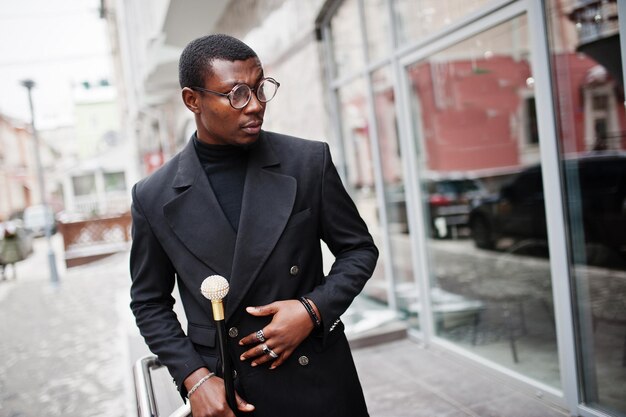 Стильный афро-американский джентльмен в элегантной черной куртке, держащий ретро-трость в качестве тростниковой фляжки или трость с золотым алмазным шариком на ручке Богатый модный афро-мужчина