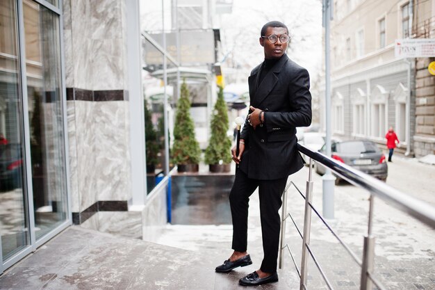 Stylish african american gentleman in elegant black jacket holding retro walking stick as cane flask or tippling cane with golden diamond ball handle Rich fashionable afro man