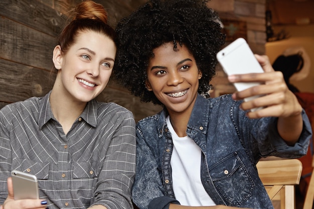 Elegante ragazza afro-americana con taglio di capelli afro che tiene mobile, prendendo selfie