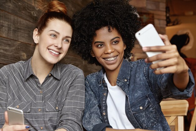 Selfieを取って、携帯電話を保持しているアフロのヘアカットとスタイリッシュなアフリカ系アメリカ人の女の子