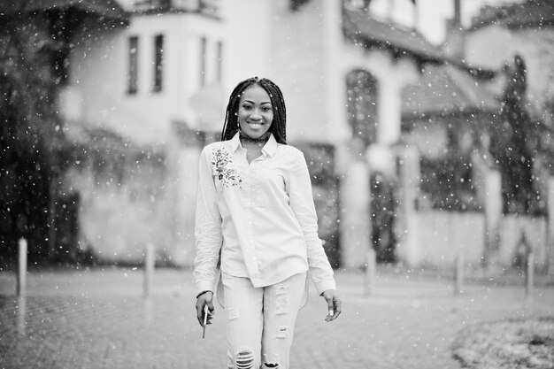 手元に携帯電話を持っている恐怖を持つスタイリッシュなアフリカ系アメリカ人の女の子屋外の雪の天気