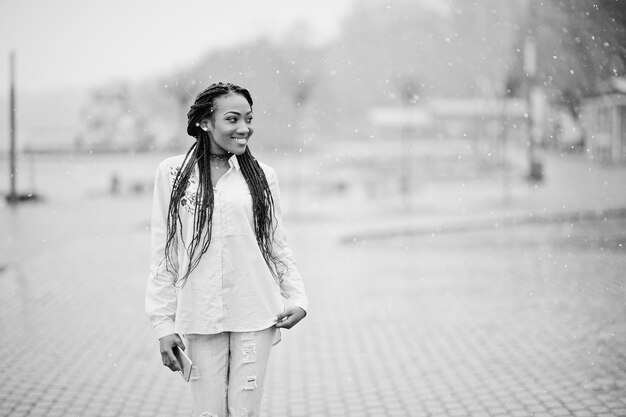 Stylish african american girl with dreads holding mobile phone at hand outdoor with snowy weather