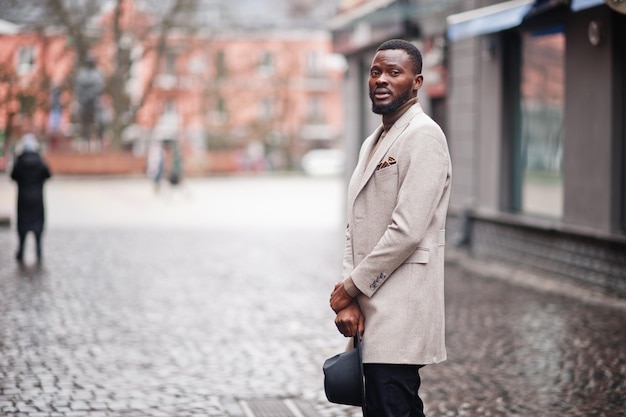 Elegante uomo afroamericano indossare giacca beige e cappello nero posa in strada