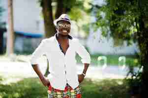 Free photo stylish african american man in white shirt and colored pants with hat and glasses posed outdoor black fashionable model boy