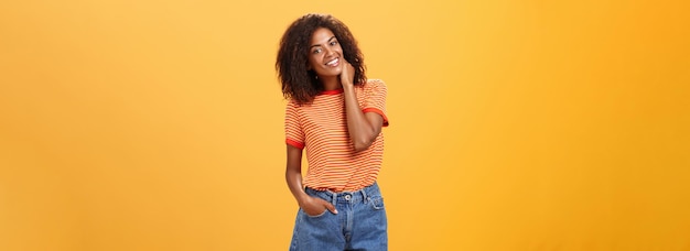 Free photo stylish african american slim woman with curly medium hair holding hand in denim shorts tilting head
