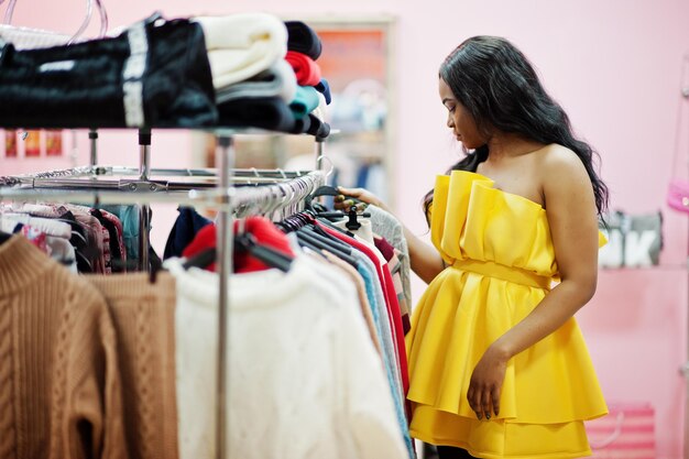 ピンクのお店でポーズをとって服を選ぶ黄色いドレスのスタイリッシュなアフリカ系アメリカ人女性