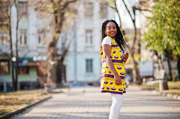 Stylish african american women in yellow jacket posed on street at sunny day with mobile phone at hand