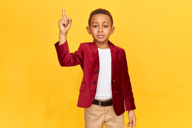 stylish Afro American schoolboy wearing elegant clothes raising fore finger as sign of drawing attention