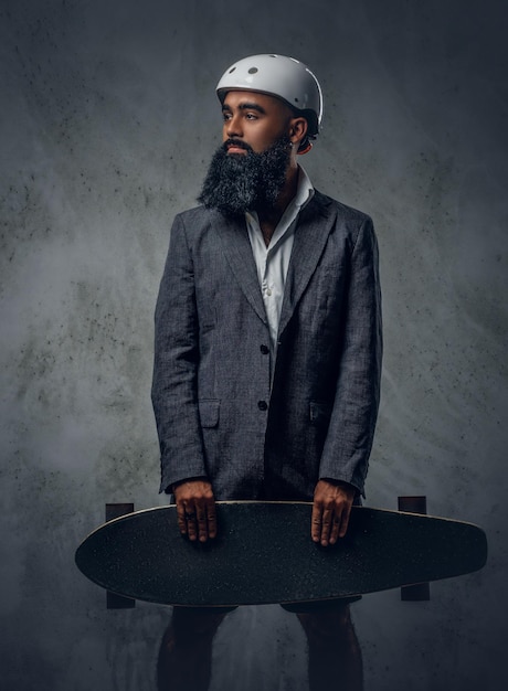 Free photo a stylish arabic male dressed in a grey suit holds long board.