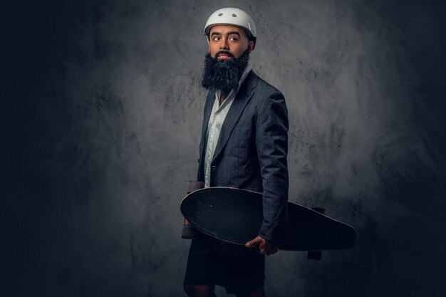 Free photo a stylish arabic male dressed in a grey suit holds long board.