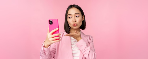 휴대 전화 앱으로 스마트폰 화상 채팅에서 셀카를 찍는 정장을 입은 세련된 아시아 여성 사업가