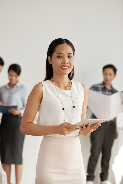 Free photo stylish asian businesswoman posing with tablet, and colleagues standing behind