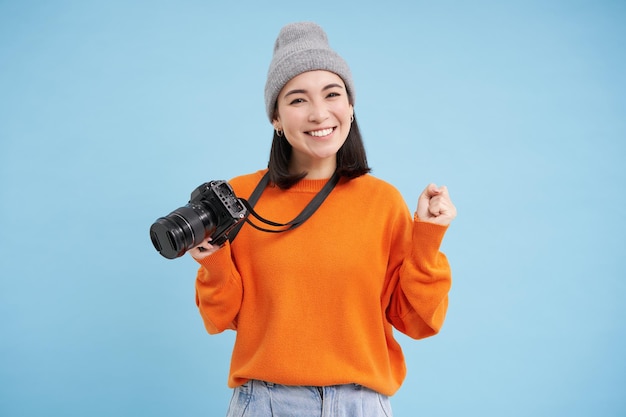 Stylish asian girl with digital camera taking pictures woman photographer smiling standing over blue