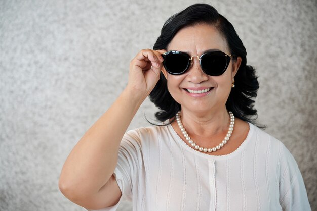 Stylish Asian woman wearing sunglasses giving a toothy smile to camera