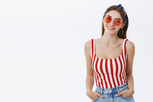 stylish attractive european female fashion woman in trendy round sunglasses headband and striped top holding hands in pockets and smiling