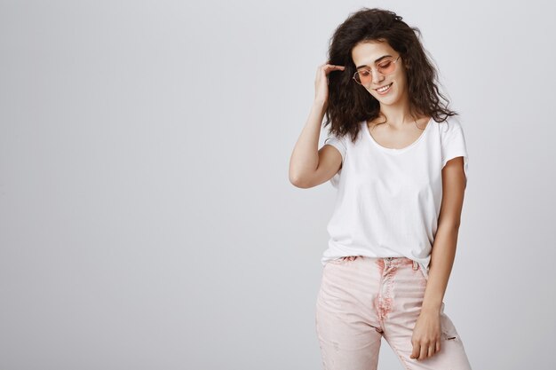 Stylish attractive woman in sunglasses posing over grey wall