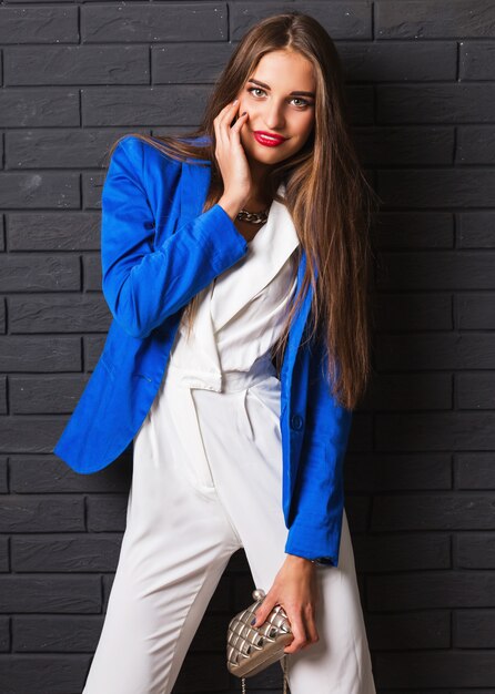 Stylish attractive young woman in casual white costume and blue jacket holding luxury purse