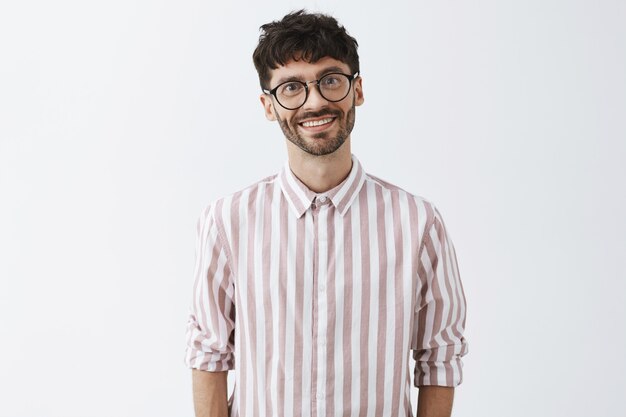 stylish bearded guy posing against the white wall with glasses