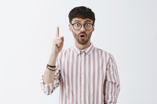 stylish bearded guy posing against the white wall with glasses