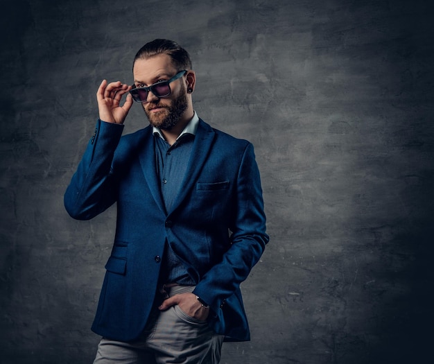A stylish bearded hipster male dressed in a suit and sunglasses over dark grey background.