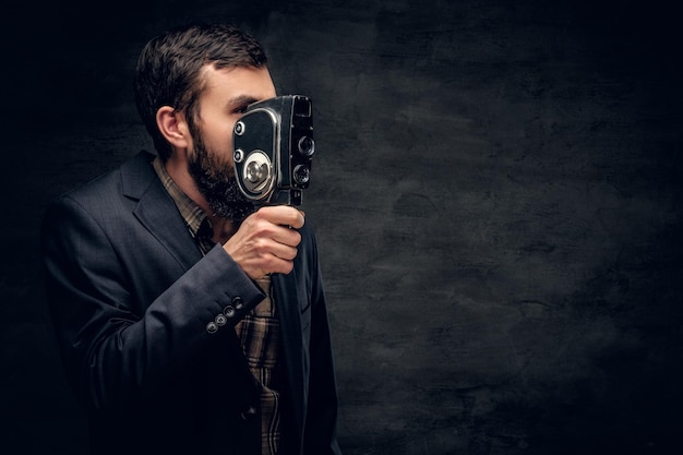 A stylish bearded male dressed in a suit holds vintage 8mm video camera.