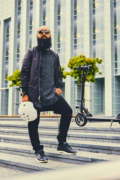 Free photo stylish bearded male on a step over electric scooter background.