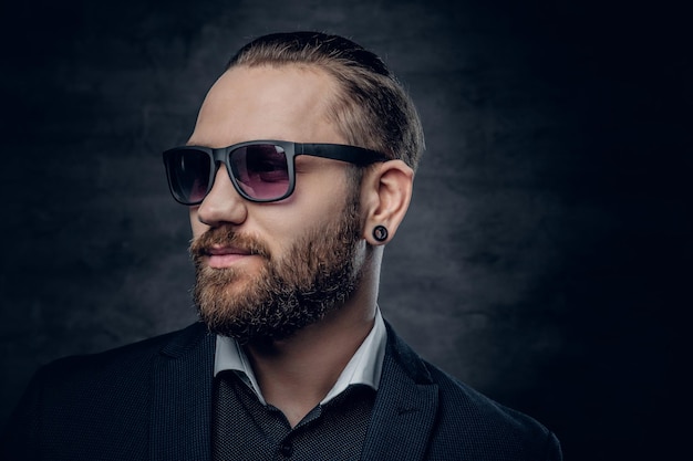 Stylish bearded male in sunglasses over dark grey background.