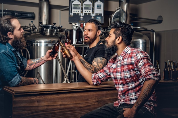 Foto gratuita elegante barbuto tatuato uomini caucasici, neri e indiani che bevono birra artigianale nel microbirrificio.